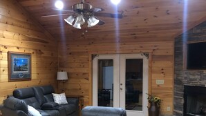 Un acogedor interior de cabaña de madera con chimenea, un ventilador de techo y un sofá para dos personas.