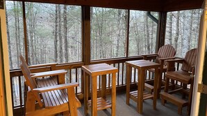 Una terraza de madera con bancos y mesas, con vistas a un área boscosa.