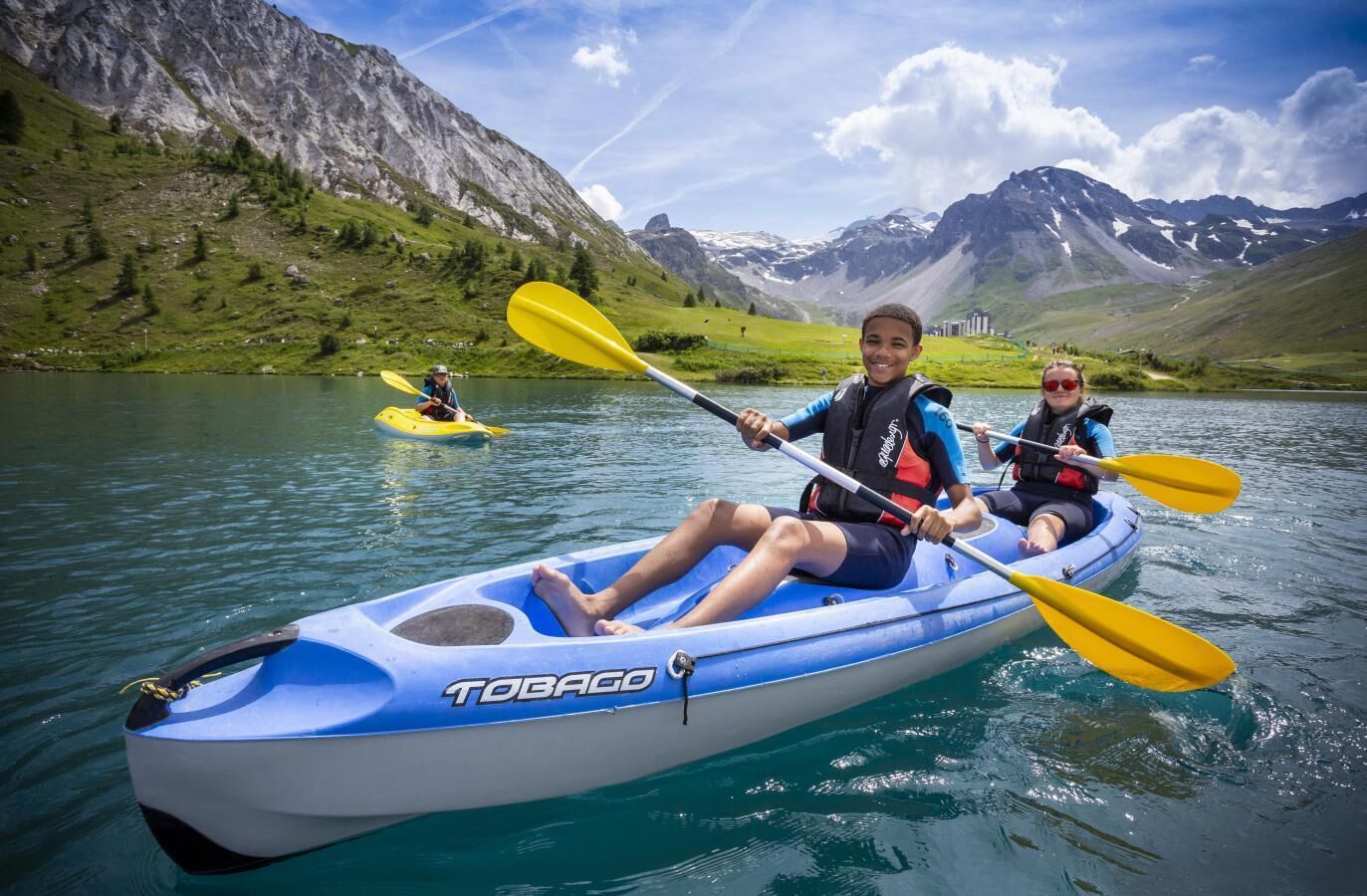 Une personne pratiquant le kayak sur un lac, avec des montagnes en arrière-plan.