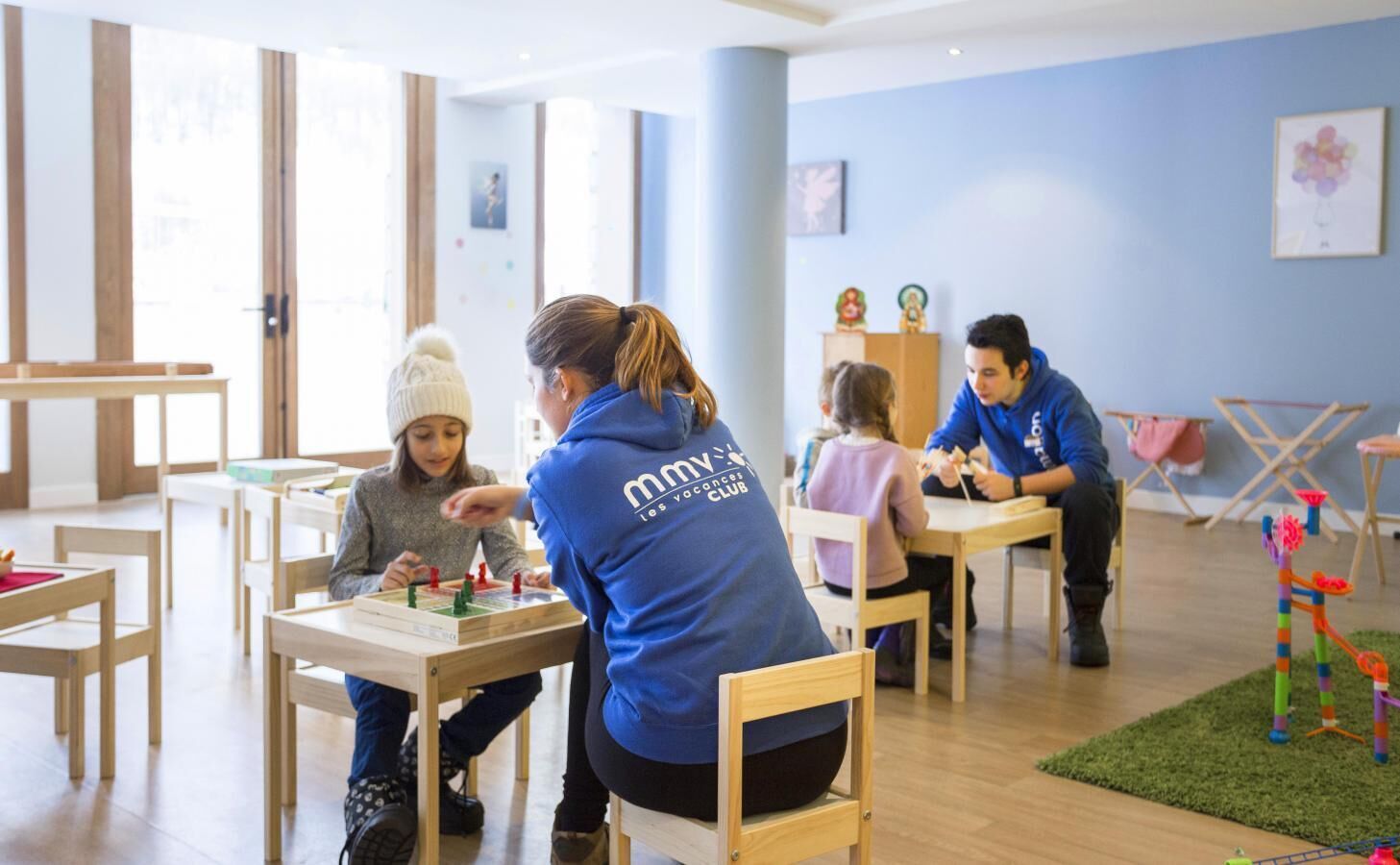A group of people engaged in activities at a brightly lit indoor space with wooden furniture and a blue wall.