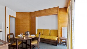 Habitación pequeña con un separador de madera, un sofá amarillo, una mesa de comedor con sillas y un taburete.