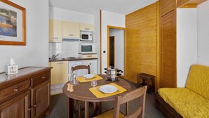 Una habitación compacta con una mesa de comedor preparada para dos personas, una cama y una kitchenette.