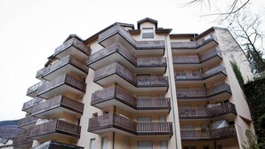 Edificio residencial de varios pisos con balcones, un centro deportivo y de recreación, y montañas al fondo.