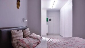 Una camera da letto con un letto, un comodino, una lampada a parete, un armadio e una porta con finestra circolare.