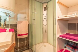 A bathroom with a glass-enclosed shower, a sink with a towel, and a shelf with towels.
