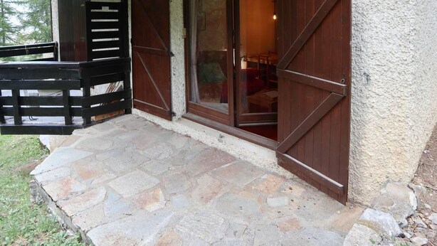 Une terrasse dallée de pierres, avec des volets en bois et un portail en bois.