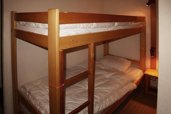 A bunk bed with two levels, a bedside table, and a wall-mounted lamp.