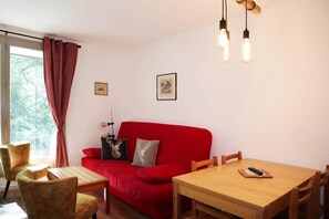 A room with a red sofa, a wooden dining table, and chairs. There are two wall-mounted light fixtures above the table. - 100m from ski slopes, 1st floor, balcony, tv, 43m², Les Orres (Les Orres)