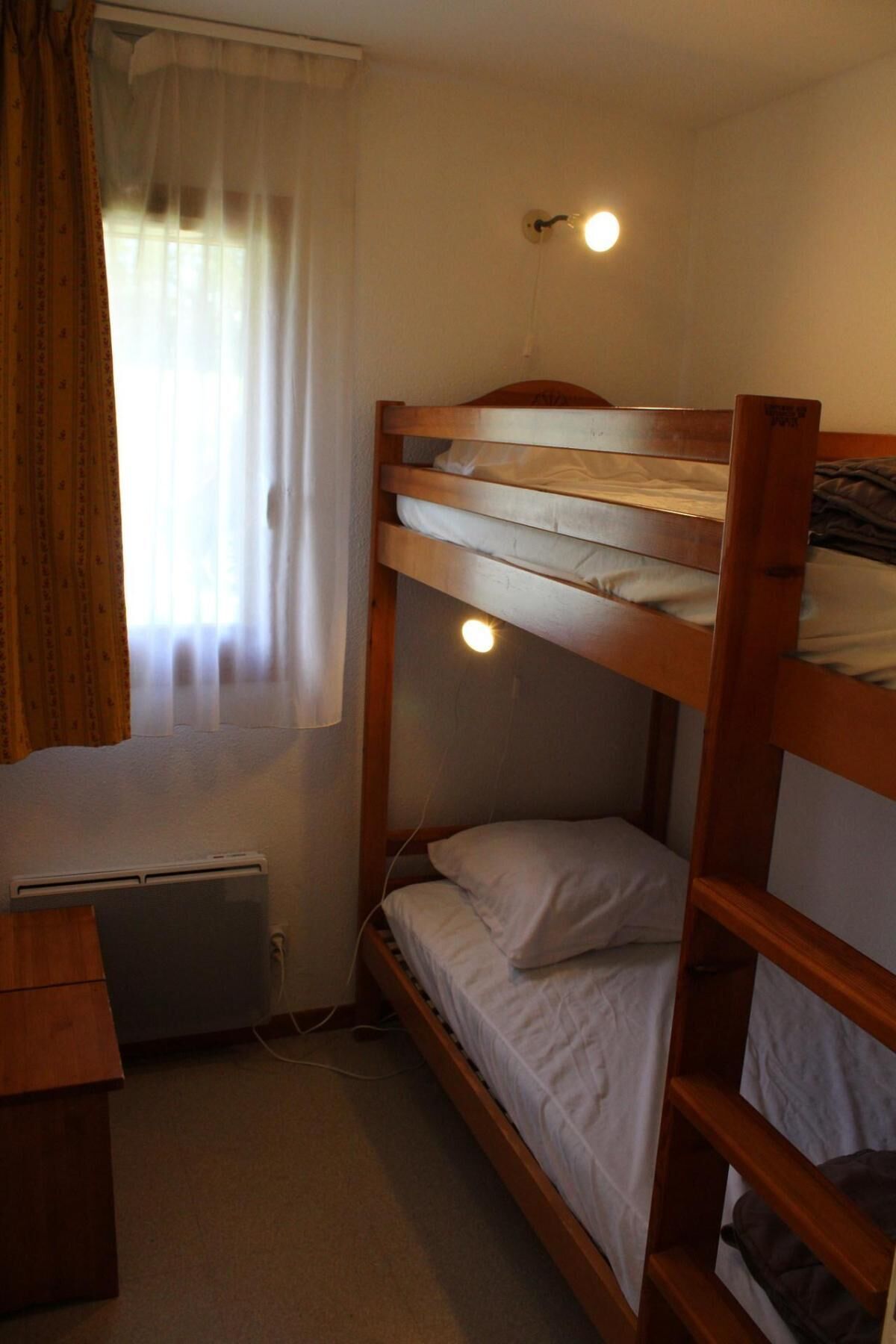 Een kleine, functionele kamer met een stapelbed, een bureau en een radiator.