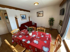 A dining area with a red tablecloth, wooden chairs, a potted plant, and a red sofa.