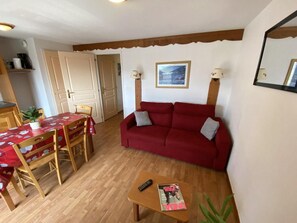 A living room with a red sofa, wooden dining table, and a small coffee table. - 1st floor, view mountain, balcony, tv, 32m², La Joue du Loup (Le Dévoluy)
