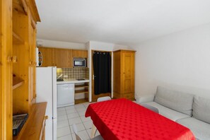 A compact living space with a kitchenette, a dining table with a red tablecloth, and a sofa. - 50m from ski slopes, 2nd floor, balcony, tv, ski locker, 35m², Valloire (Valloire)