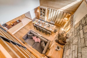 A spacious loft-style living area with a dining table set for six, a cozy seating area with a sofa, and a stone wall.