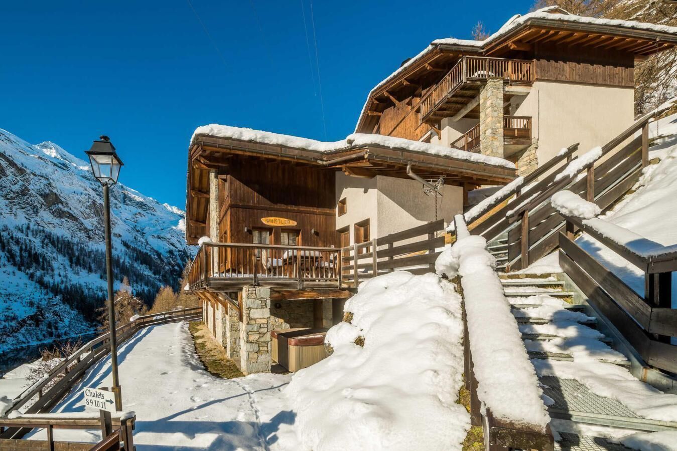 A wooden chalet with a balcony, surrounded by snow-covered mountains and a clear sky.