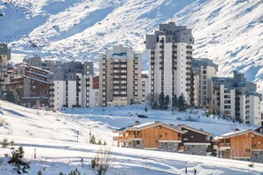 A snow-covered mountainous area with modern multi-story buildings, likely a ski resort.