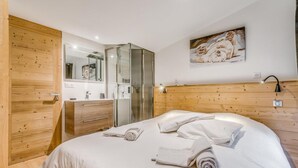 Ein Schlafzimmer mit einem hölzernen Kopfteil, einem Bett mit weißer Bettwäsche, einer Duschkabine aus Glas und einem Bild an der Wand.