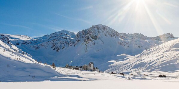 A snow-covered mountain landscape with a ski resort, including buildings and ski slopes.