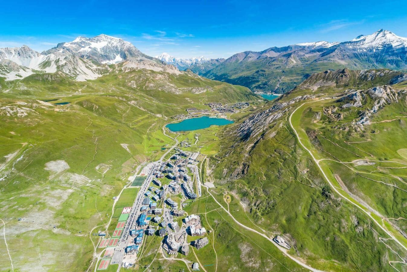 An aerial view of a mountainous area with a lake, roads, and a cluster of buildings.