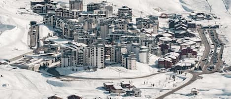 A snow-covered mountainous area with a cluster of buildings, including hotels and possibly residential structures, surrounded by ski slopes and a winding road.