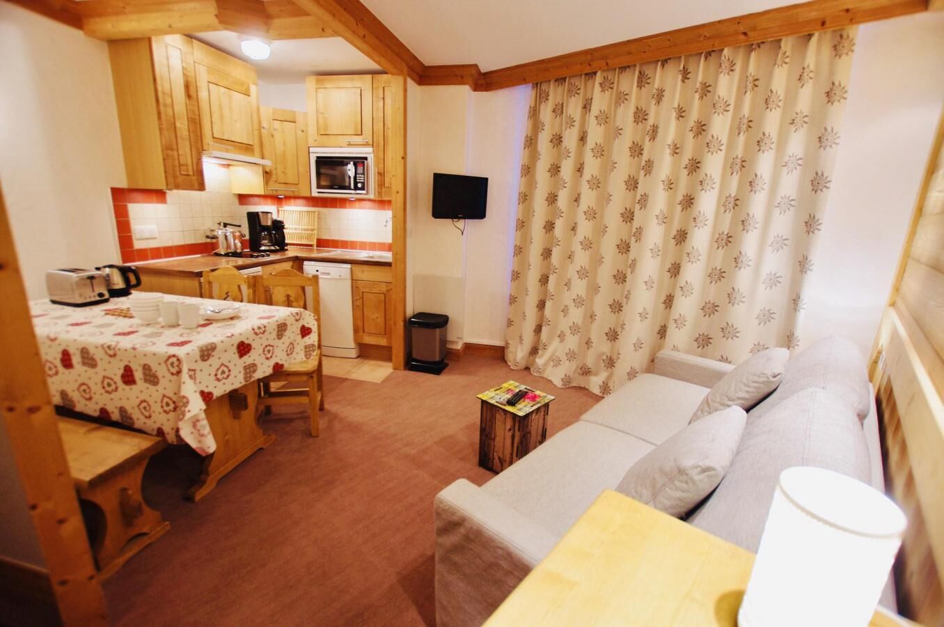 A cozy room with a wooden dining table, a sofa, and a kitchen area with wooden cabinets and a microwave.