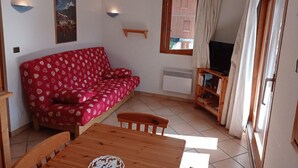 A cozy living room with a red patterned sofa, a wooden dining table, and a television set. - 200m from ski slopes, 3rd floor, view mountain, balcony, tv, ski locker, 36m², Champagny-en-Vanoise (Champagny-en-Vanoise)