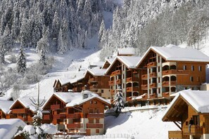 Eine schneebedeckte Lodge mit mehreren Holzbauten, Balkonen und einer Skipiste im Hintergrund.