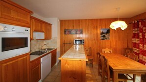 A kitchen with wooden cabinets, a built-in oven, a microwave, and a tiled island. - 250m from ski slopes, Ground floor, terrace, balcony, tv, ski locker, 65m², Champagny-en-Vanoise (Champagny-en-Vanoise)