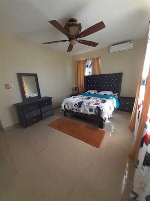 A bedroom with a bed, a dresser, a ceiling fan, and a window with curtains.