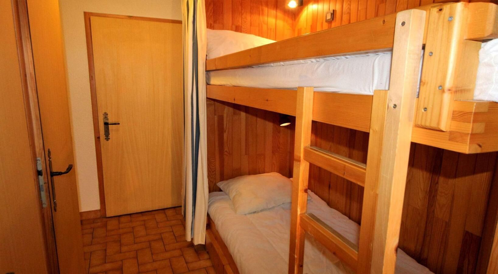 Une chambre avec des lits superposés, une porte en bois et un plancher en briques.