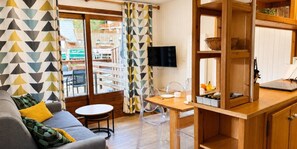 A room with a sofa, a dining table, chairs, a TV, and a view of an outdoor area with a cinema. - 50m from ski slopes, 1st floor, terrace, tv, 35m², Champagny-en-Vanoise (Champagny-en-Vanoise)
