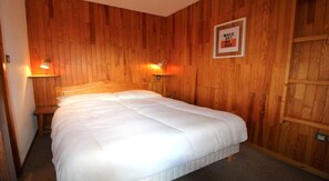 A bedroom with a wooden wall, a bed with white bedding, two wall-mounted lamps, and a framed sign on the wall.