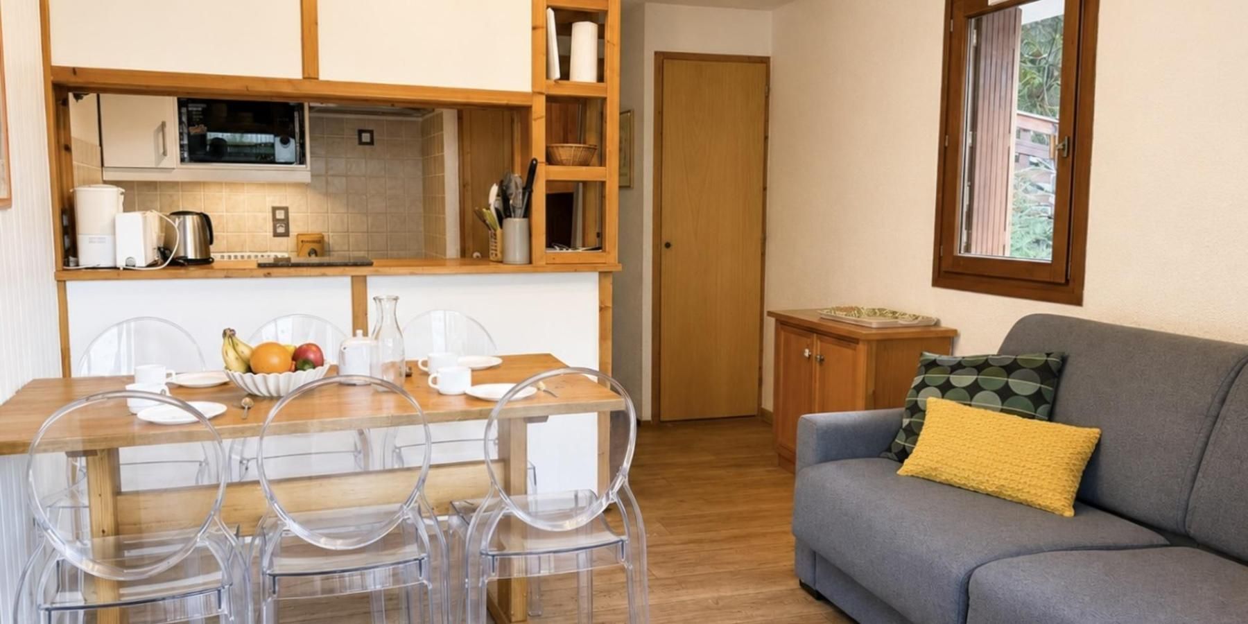 A compact living space with a dining area, kitchenette, and a sofa with a cushion.