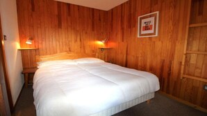 A neatly made bed in a room with wooden walls and two wall-mounted lamps. - 50m from ski slopes, 1st floor, terrace, tv, 35m², Champagny-en-Vanoise (Champagny-en-Vanoise)