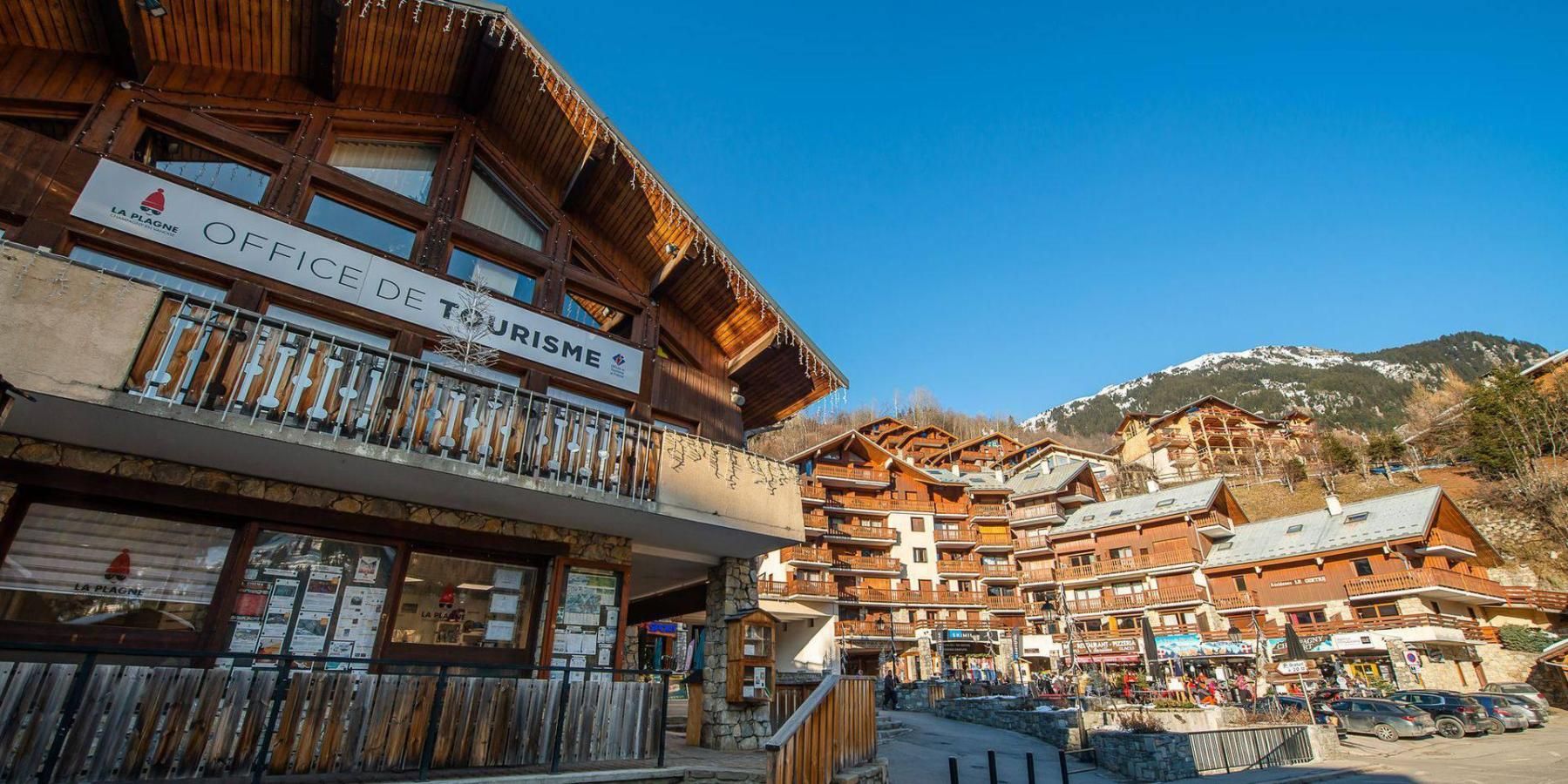 A wooden building with balconies, a sign for 'OFFICE DE TOURISME,' and a mountainous backdrop.
