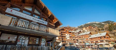 A wooden building with balconies, a sign for 'OFFICE DE TOURISME,' and a mountainous backdrop.