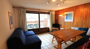 A room with a wooden table, a sofa, a TV, and a window with curtains. - 50m from ski slopes, 1st floor, terrace, tv, 35m², Champagny-en-Vanoise (Champagny-en-Vanoise)
