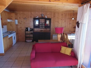 A compact living space with a red sofa, a wooden cabinet with a star decoration, a small kitchen area, and a window with curtains.