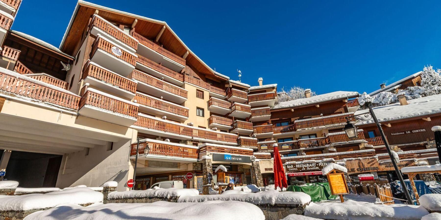 Un hôtel à plusieurs étages doté de balcons, d’une enseigne indiquant un service de location de matériel de ski et d’un restaurant.