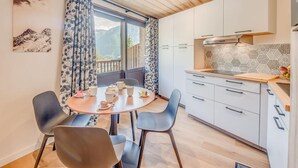 A modern kitchen with a dining area, featuring a round table, chairs, and a view of mountains through the window. - Resort center, 4th floor, balcony, tv, 29m², Champagny-en-Vanoise (Champagny-en-Vanoise)
