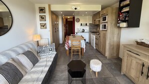 A cozy living room with a sofa, a coffee table, and a dining table set for four. A kitchen with wooden cabinets and a microwave is visible in the background. - 100m from ski slopes, 1st floor, view ski slopes, balcony, tv, ski locker, 28m², Les Saisies (Les Saisies)