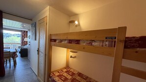 A bunk bed with a patterned bedspread, a small table with chairs, and a view of the outdoors through a door. - 100m from ski slopes, 1st floor, view ski slopes, balcony, tv, ski locker, 28m², Les Saisies (Les Saisies)