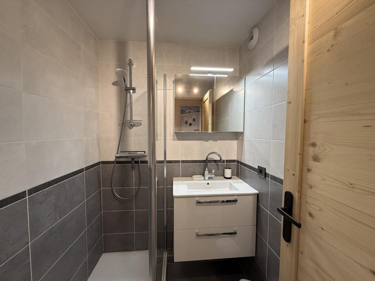 A modern bathroom with a glass-enclosed shower, a white sink, and a wooden door.