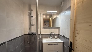 A modern bathroom with a glass-enclosed shower, a white sink, and a wooden door. - 100m from ski slopes, 1st floor, view ski slopes, balcony, tv, ski locker, 28m², Les Saisies (Les Saisies)