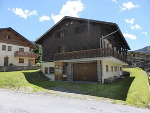 Een houten tweegevelwoning met balkon, garage en een klein voortuintje.