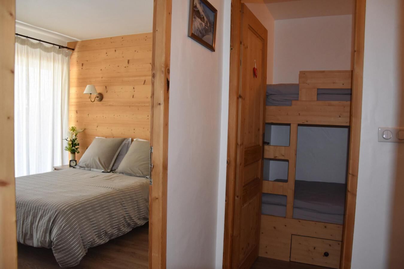 A bedroom with a wooden headboard, a bed with a striped bedspread, a bedside lamp, and a small plant.