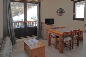 A room with a wooden dining table, a TV on a dresser, and a view of a snowy outdoor area through a sliding door.