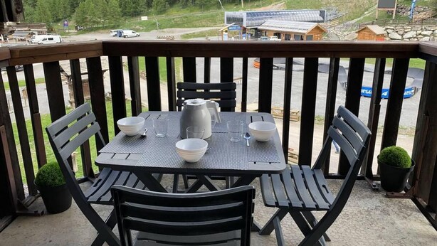 A balcony with a table set for four, overlooking a mountainous area with a road and buildings in the distance.