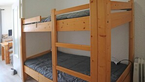 A bunk bed with a desk and chair in a room with white walls and a radiator.