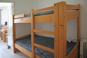 A bunk bed with a desk and chair in a room with white walls and a radiator.