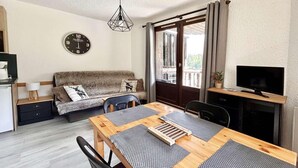 A cozy room with a wooden dining table, a sofa, a TV, and a clock on the wall.